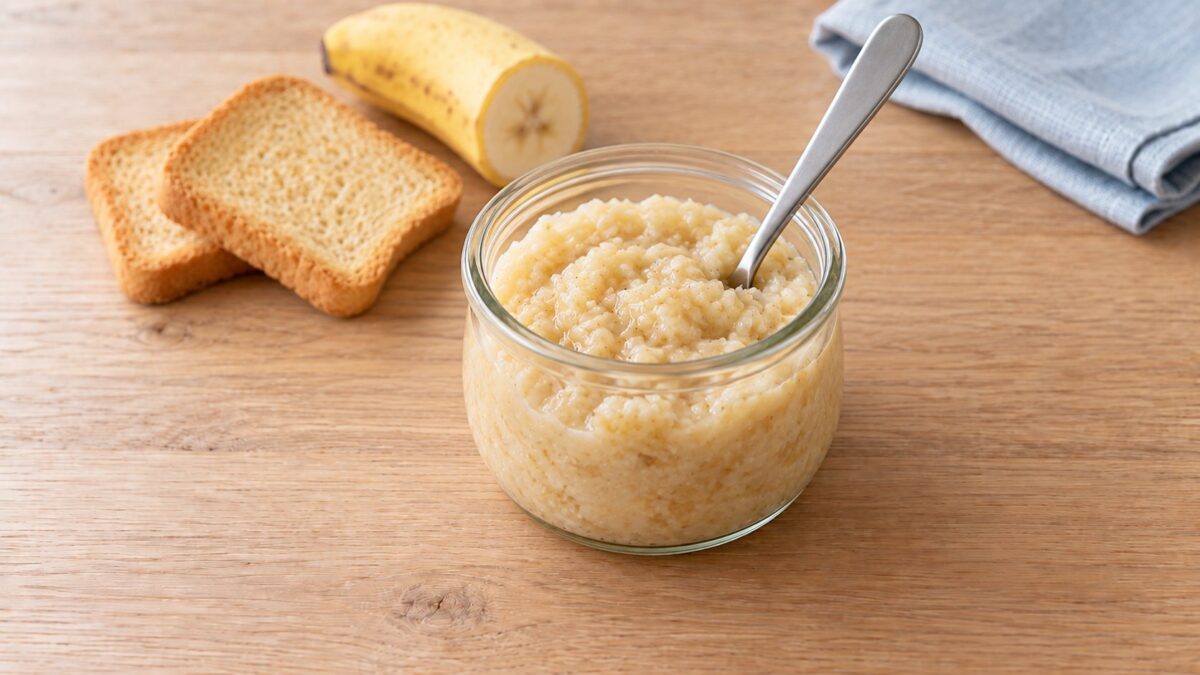 KI-generiertes Symbolbild: Zwiebackbrei mit Banane in einem kleinen Glas, dahinter Zwieback und Banane